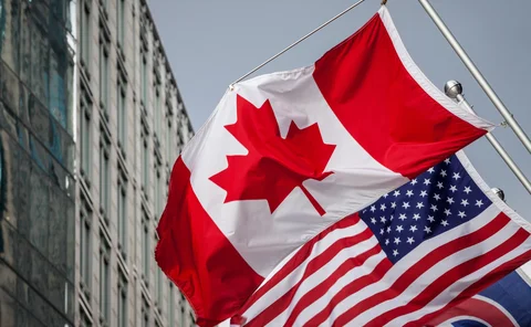Picture of the canadian flag joint with and american stars and stripes flag taken in front of a cold and blue business building in the CDB of Toronto. Toronto is the biggest city of Canada, and a major hub for economy, politics and business in America.