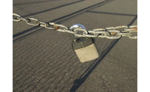 metal-padlock-and-chain-stretched-across-fence-shadow