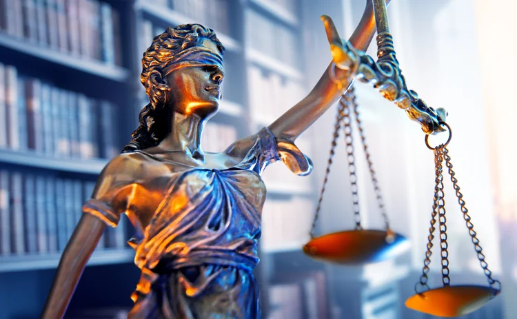 Lady justice stands in a law office with a bookshelf of law books out of focus in the background.