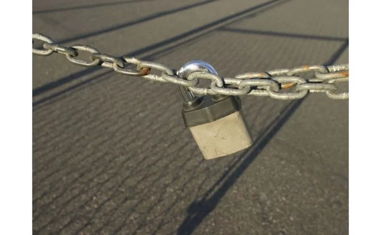 metal-padlock-and-chain-stretched-across-fence-shadow