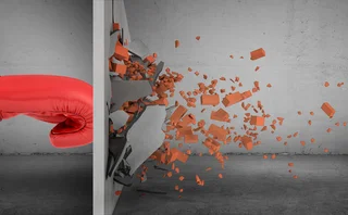 Red boxing glove punching through a concrete wall, sending bricks and debris flying in all directions in a dramatic, high-impact scene symbolising strength and breakthrough