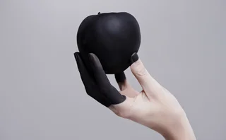 Studio shot of a woman's hand holding a black apple
