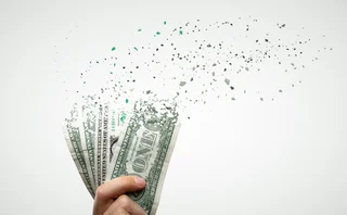 A hand holding several dollar notes with the tops of the banknotes crumbling and flying away in particles.