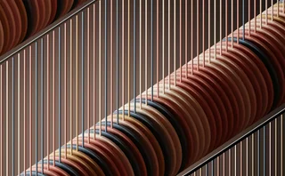 Abstract geometric artwork with stacked circular discs and vertical lines in earthy tones of red, brown, beige and black, creating a modern architectural pattern.