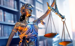 Lady justice stands in a law office with a bookshelf of law books out of focus in the background.