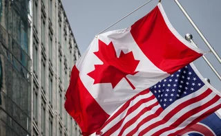 Picture of the canadian flag joint with and american stars and stripes flag taken in front of a cold and blue business building in the CDB of Toronto. Toronto is the biggest city of Canada, and a major hub for economy, politics and business in America.