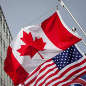 Picture of the canadian flag joint with and american stars and stripes flag taken in front of a cold and blue business building in the CDB of Toronto. Toronto is the biggest city of Canada, and a major hub for economy, politics and business in America.